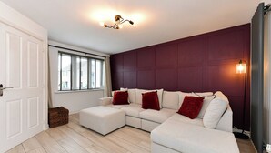 Una sala moderna con sofá modular, una ventana con persianas, una lámpara de pie y una puerta.