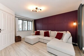 Ein modernes Wohnzimmer mit Ecksofa, einem Fenster mit Jalousien, einer Stehlampe und einer Tür.