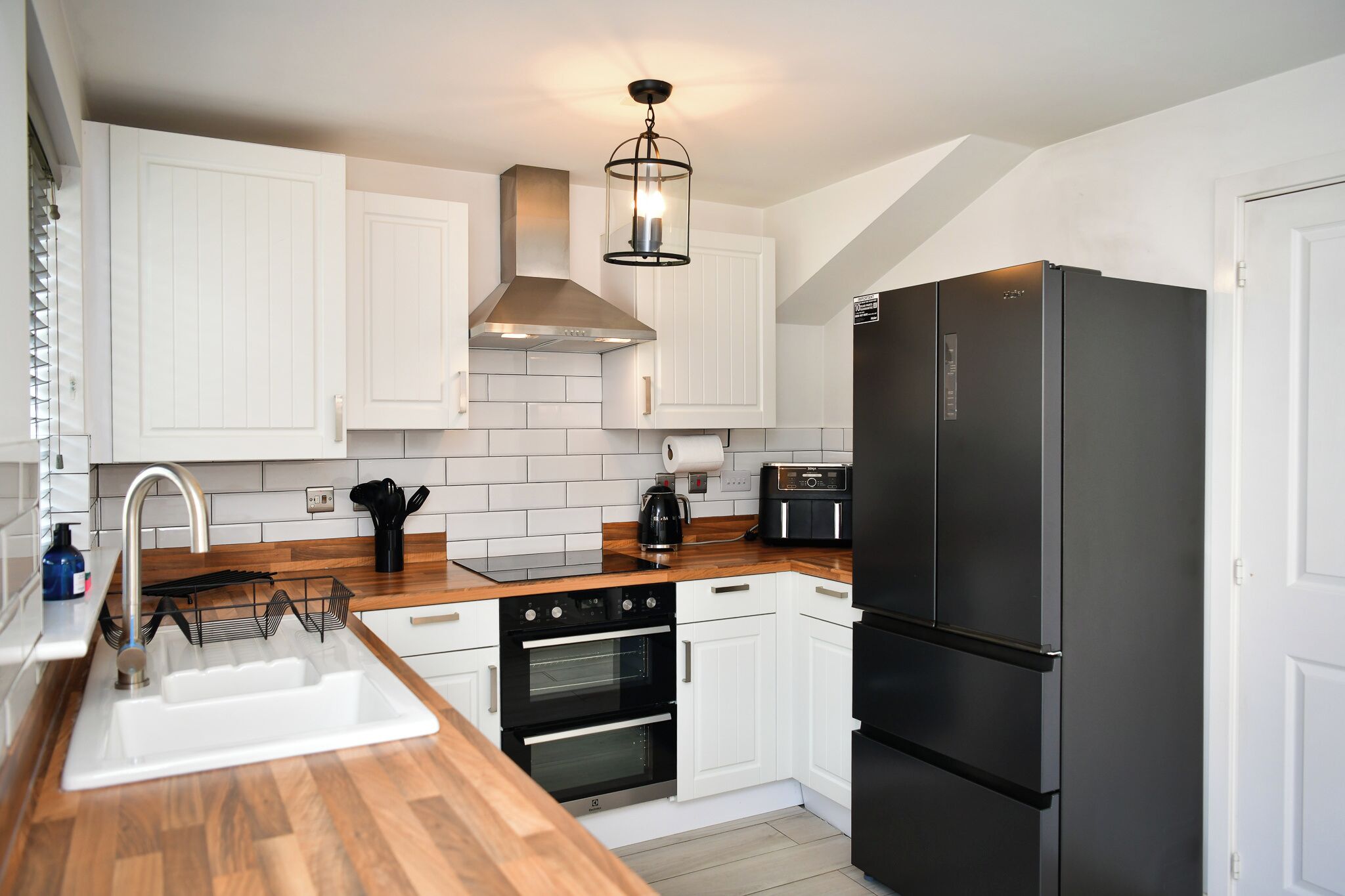 A modern kitchen with white cabinets, a black refrigerator, and a wooden countertop.