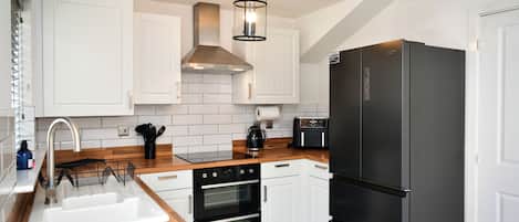 A modern kitchen with white cabinets, a black refrigerator, and a wooden countertop.
