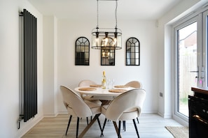 A dining area with a round table, four chairs, a chandelier, and a window with a view. - Stylish Family Home with Garden & Free Parking - Pass the Keys (Cardiff)