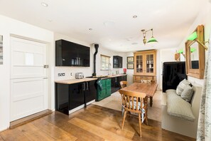 A compact kitchen with a dining area, wooden flooring, and a built-in TV. - Charming Countryside Cottage with a Private Garden - Pass the Keys (Henley-in-Arden)