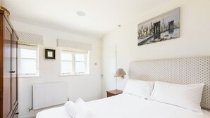 Ein Schlafzimmer mit einem Bett, einem Nachttisch, einer Lampe, einem Heizkörper, einem Kleiderschrank und einem Fenster mit Vorhängen.