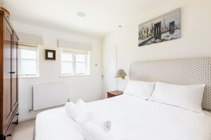 A bedroom with a bed, a nightstand, a lamp, a radiator, a wardrobe, and a window with curtains. - Charming Countryside Cottage with a Private Garden - Pass the Keys (Henley-in-Arden)