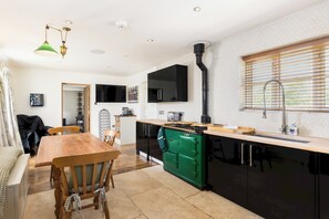 A compact kitchen with a dining area, a green stove, and a black refrigerator. - Charming Countryside Cottage with a Private Garden - Pass the Keys (Henley-in-Arden)