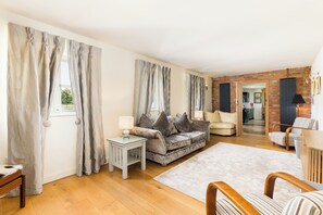 En stue med en sofa, et sofabord og et tæppe. Der er en dør, der fører til et andet rum.