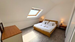 Ein Schlafzimmer mit Dachfenster, einem Bett mit Kissen, Nachttischen mit Lampen und einer hölzernen Bank.