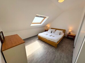Ein Schlafzimmer mit Dachfenster, einem Bett mit Kissen, Nachttischen mit Lampen und einer hölzernen Bank.