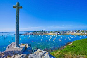 Eine Küstenansicht mit einem markanten Kreuz, klarem blauen Wasser und einer Stadt im Hintergrund.