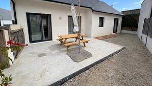 Ein modernes Haus mit Terrasse, einem Holztisch und einem überdachten Bereich.