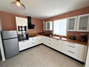 A modern kitchen with white cabinets, a built-in oven, a microwave, and a coffee maker. - KER MOAN, New house for a family in town centre (Milizac-Guipronvel)