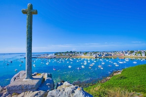 A coastal scene with a prominent cross, clear blue water, and a town in the background. - KER MOAN, New house for a family in town centre (Milizac-Guipronvel)