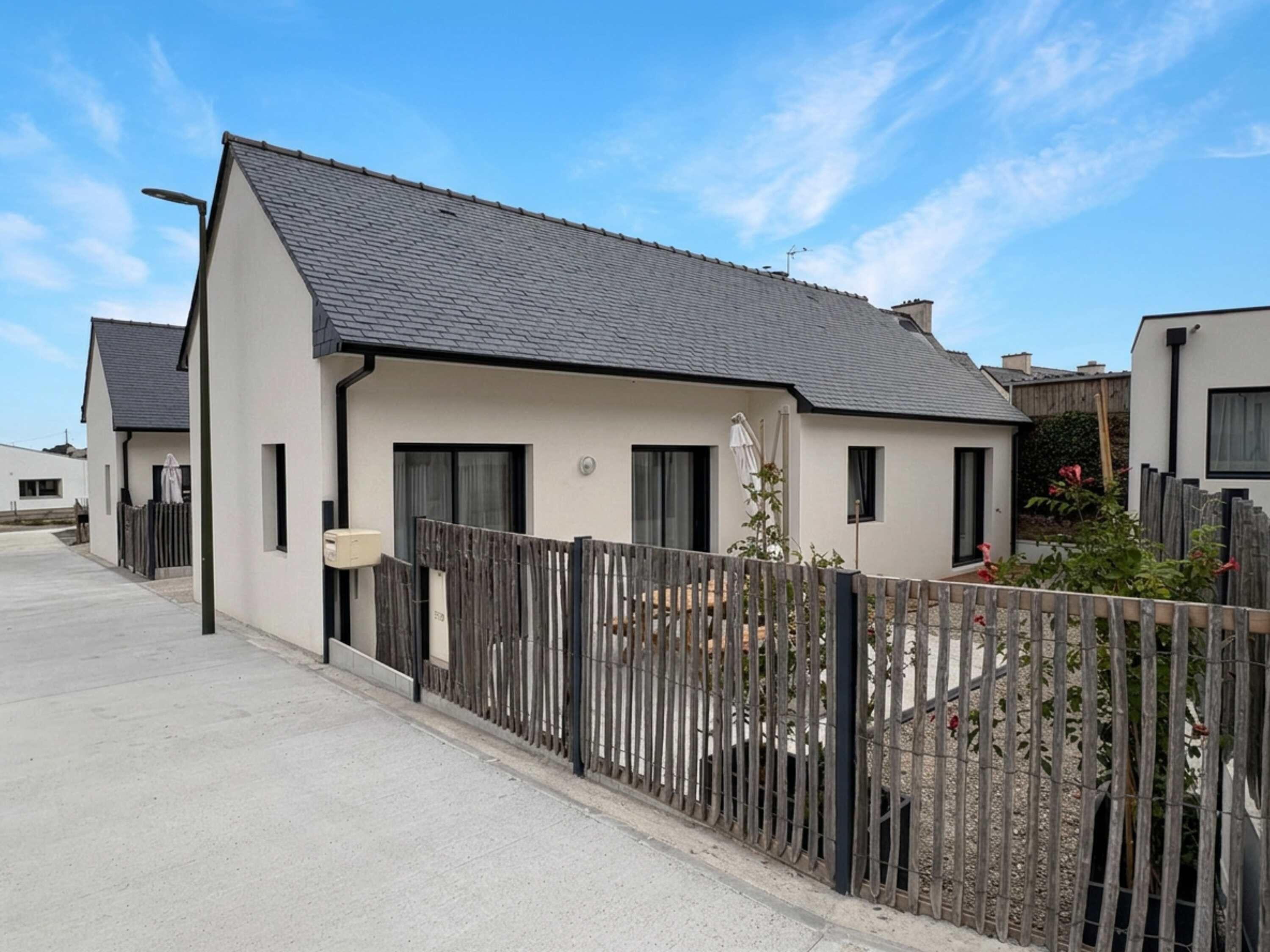 A modern two-story residential building with a sloped roof and a fenced backyard.