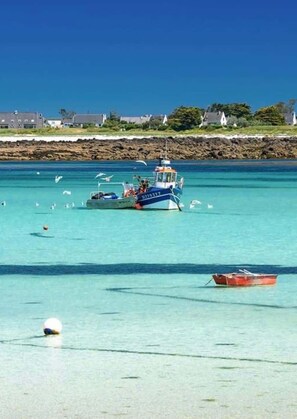 A coastal scene with a boat, clear turquoise water, and a rocky shoreline with buildings. - KER MOAN, New house for a family in town centre (Milizac-Guipronvel)