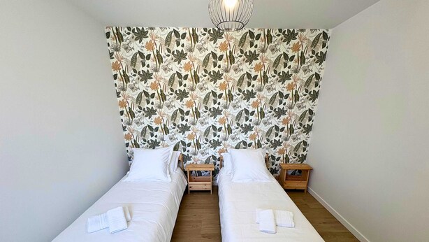 Ein Zimmer mit zwei Holzbetten, weißer Bettwäsche und einem floralen Wandmuster.