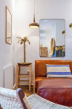 Ein Zimmer mit einem braunen Ledersofa, einem kleinen Holzschemel, einer dekorativen Zimmerpalme, einem Spiegel und einer hängenden Pendelleuchte.