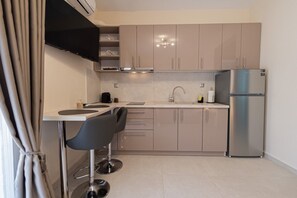 A modern kitchen with a sink, two chairs, a refrigerator, and a flat-screen TV. - SnJ Studio No2 by RentalsPro - Nea Flogita Halkidiki (Nea Flogita)