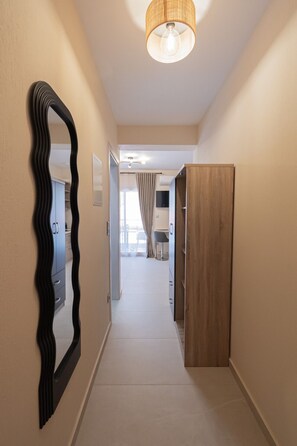 A hallway with a mirror, a wooden wardrobe, and a ceiling light fixture. - SnJ Studio No2 by RentalsPro - Nea Flogita Halkidiki (Nea Flogita)