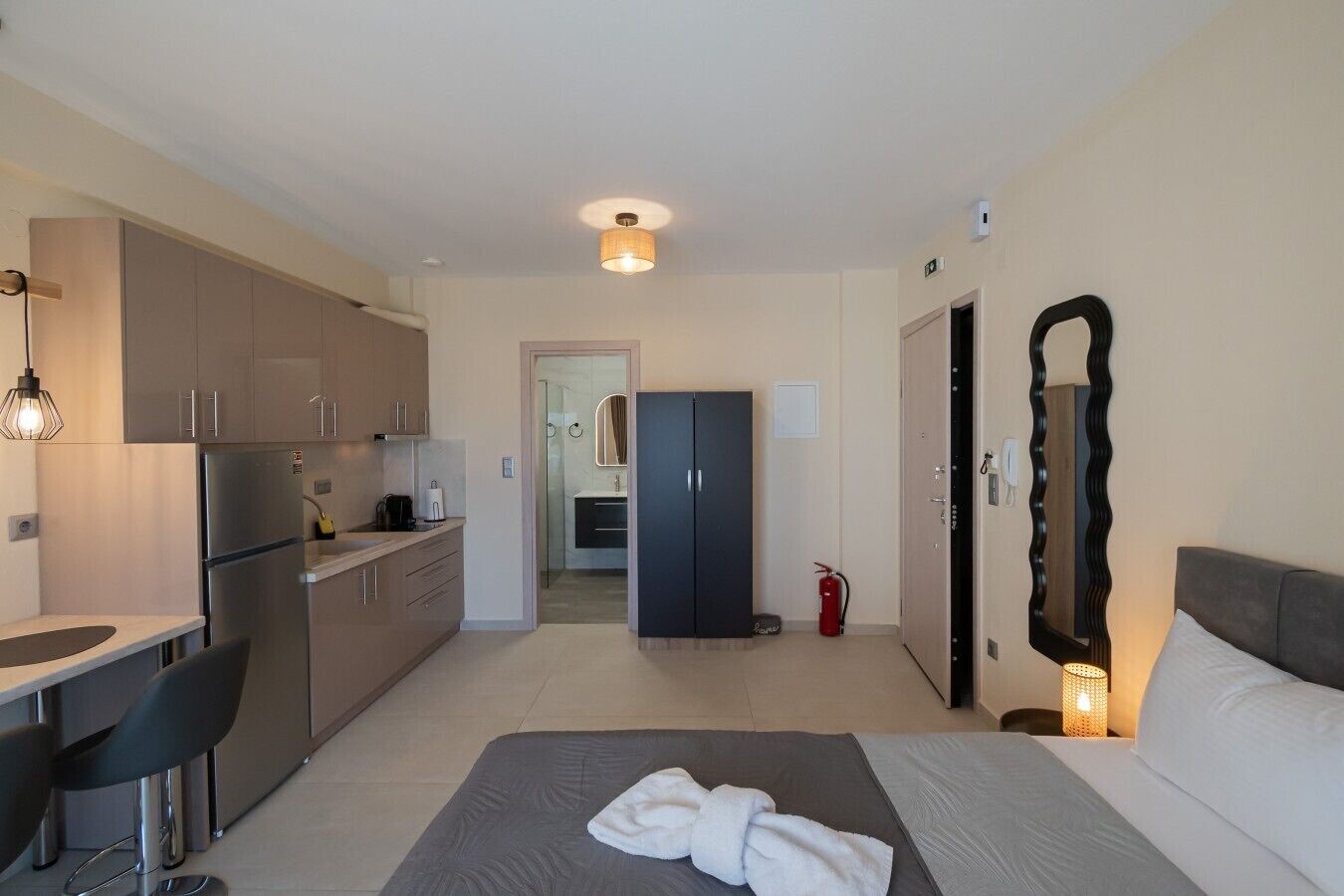 A modern hotel room with a kitchenette, a bed, a bathroom, and a mirror.