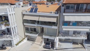 Un immeuble à plusieurs étages doté de balcons, de panneaux solaires et d’une voiture garée devant.