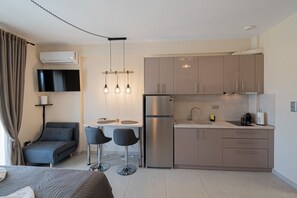 A modern kitchen with a built-in refrigerator, a dining area with two chairs, and a flat-screen TV mounted on the wall. - SnJ Studio No1 by RentalsPro - Nea Flogita Halkidiki (Nea Flogita)