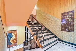 A staircase with a wooden handrail and black balusters, leading to a room with a patterned wall and a poster. - Classic Hotel Bidisha (Kanthi)