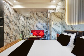Habitación de hotel con pared de mármol, cama con ropa de cama blanco y negro, sofá rojo y mesa de comedor con sillas.