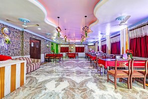 A spacious dining area with a marble floor, multiple tables set for dining, and a variety of ceiling designs. - Classic Hotel Bidisha (Kanthi)