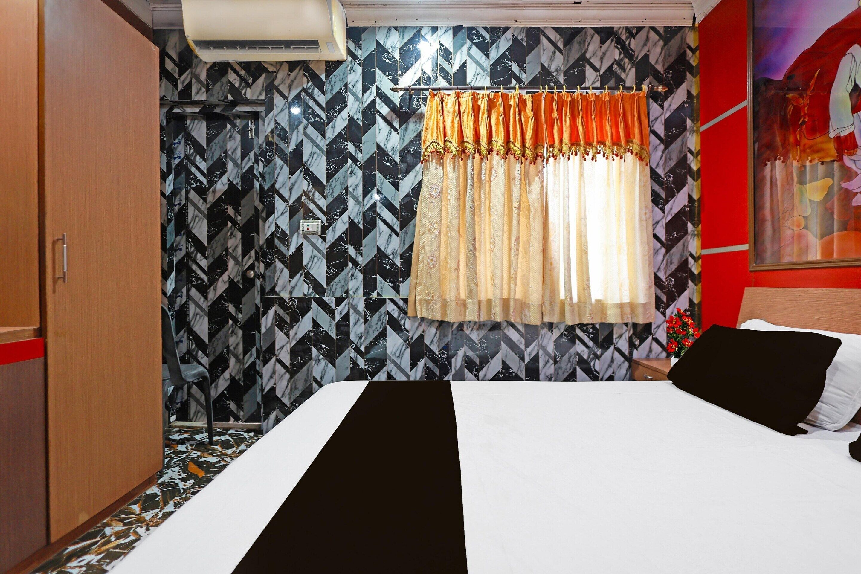 A hotel room with a bed, a wardrobe, a window with curtains, and a patterned wall.