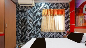 Una habitación de hotel con cama, armario, ventana con cortinas y pared con diseño.
