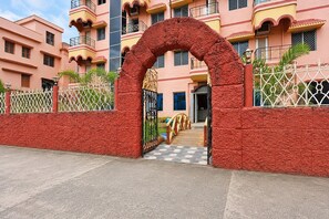 A gated entrance with a red textured wall, a metal gate, and a pathway leading to a building with balconies. - Classic Hotel Bidisha (Kanthi)
