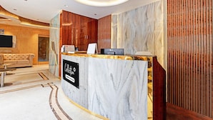 Zona de recepción de un hotel con mostrador de mármol, ventilador de techo y pared de madera.
