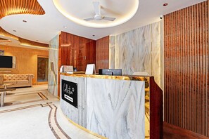 Zona de recepción de un hotel con mostrador de mármol, ventilador de techo y pared de madera.