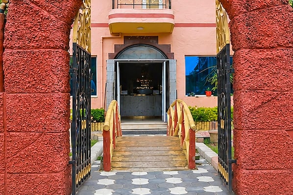 A building entrance with a staircase leading to a door, flanked by textured columns and a patterned floor.