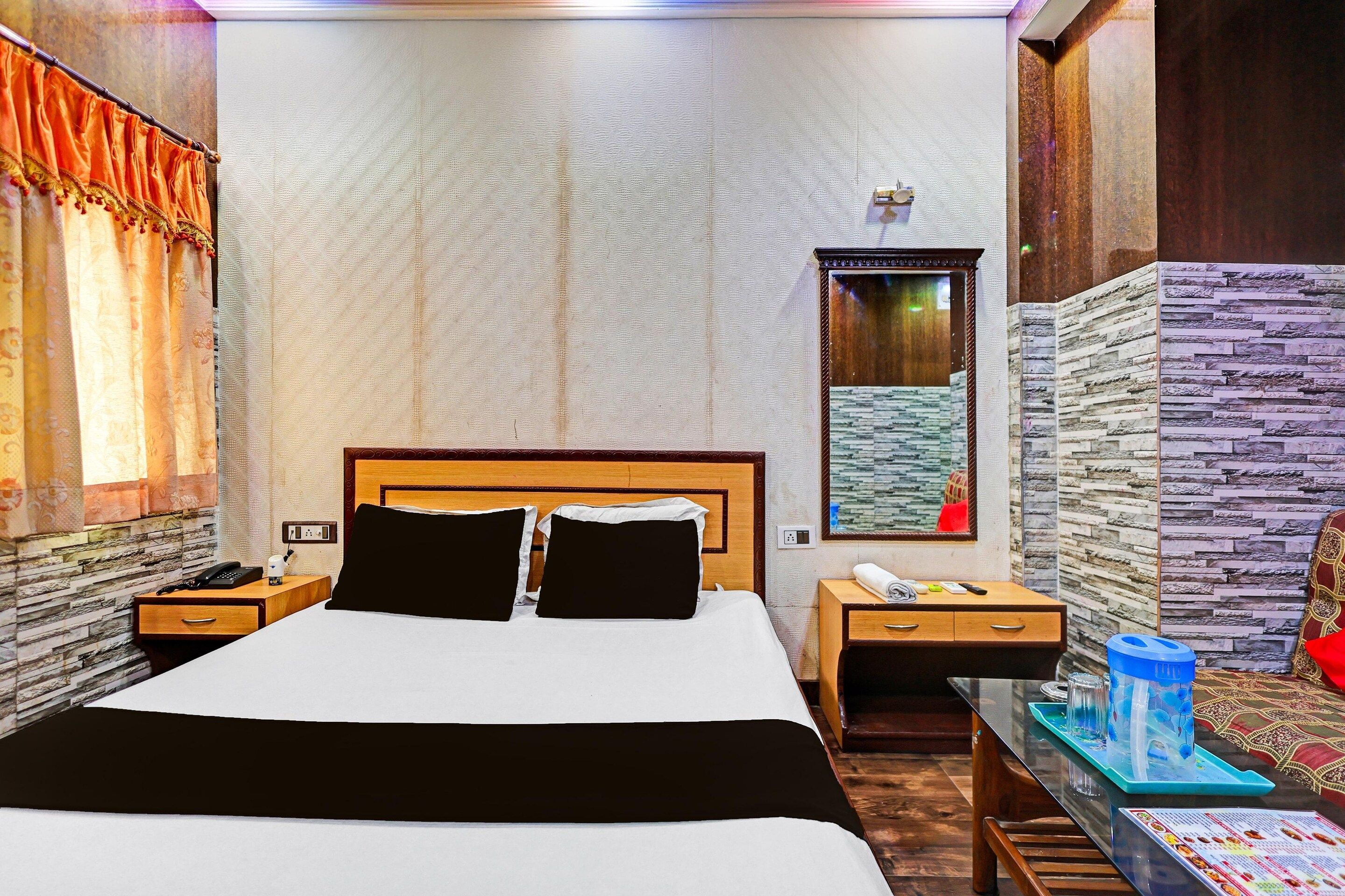 A hotel room with a large bed, a bedside table with a phone, a nightstand, a mirror, a window with curtains, and a wall with a textured pattern.