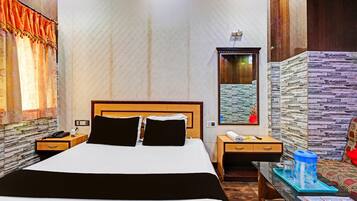 A hotel room with a large bed, a bedside table with a phone, a nightstand, a mirror, a window with curtains, and a wall with a textured pattern.
