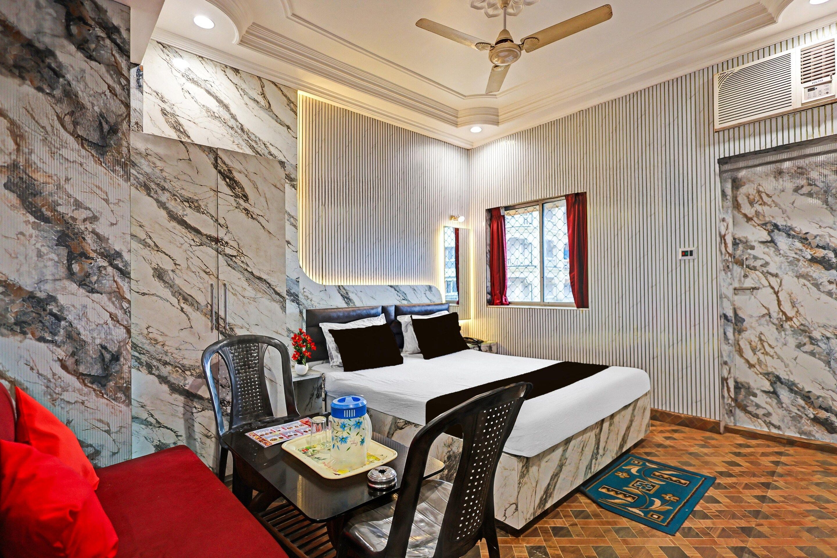 A hotel room with a bed, a desk with a chair, a window with curtains, and a ceiling fan.
