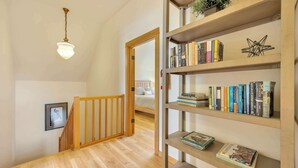 Eine Holztreppe mit Geländer führt zu einem Schlafzimmer mit Bett und einer Bücherwand voller Bücher.