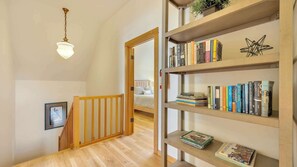Eine Holztreppe mit Geländer führt zu einem Schlafzimmer mit Bett und einer Bücherwand voller Bücher.
