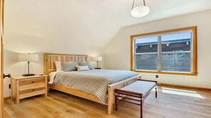 Een slaapkamer met een houten bed, nachtkastjes, een bankje en een groot raam.