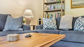 A living room with a grey sofa, patterned cushions, a wooden coffee table with a decorative bird, a lamp, and a bookshelf. - Pelican Perch by Manzanita Beach Getaway- Walk to Beach & Downtown, Dog-Friendly (Manzanita)