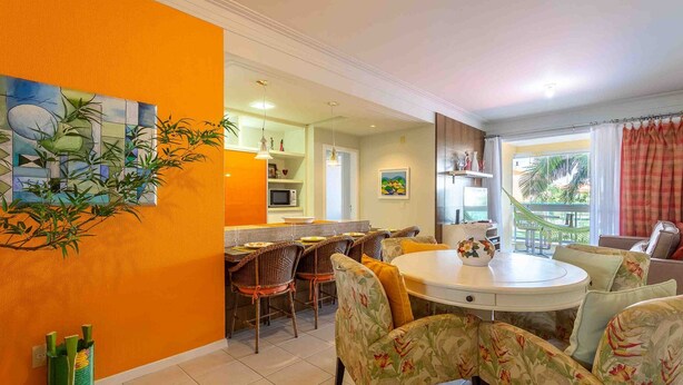 A dining area with a round table and chairs, a kitchen in the background, and a living area with a sofa and a window. - Comfortable Beachside Apartment in Floripa Rvg101 (Florianópolis)