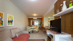 A living room with a sofa, a TV, and a dining area with chairs and a table. - Comfortable Beachside Apartment in Floripa Rvg101 (Florianópolis)