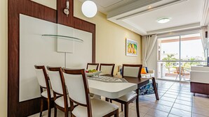 Un coin repas avec une table dressée pour quatre personnes, entourée de chaises en bois. Un luminaire est fixé au mur au-dessus de la table, et un tableau orne le mur.