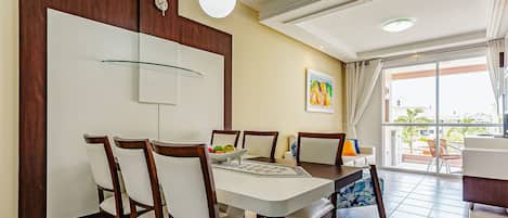 Un comedor con una mesa dispuesta para cuatro personas, rodeada de sillas de madera. Hay una lámpara de pared sobre la mesa y un cuadro en la pared.