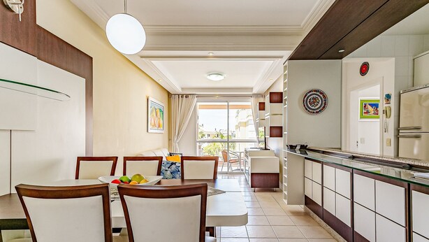 Un coin repas avec une table et des chaises, une cuisine équipée de placards et d’un réfrigérateur, et une vue sur l’extérieur par une porte vitrée.
