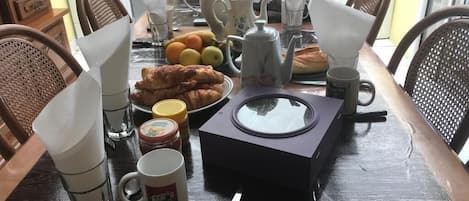 A breakfast table with a teapot, cups, a mug, and a plate of croissants.