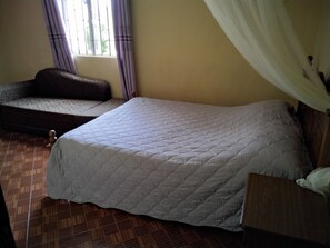 A room with a bed, a sofa, a window with curtains, and a wooden floor. - Marjolaine Bed and Breakfast (Lourdes (65100))