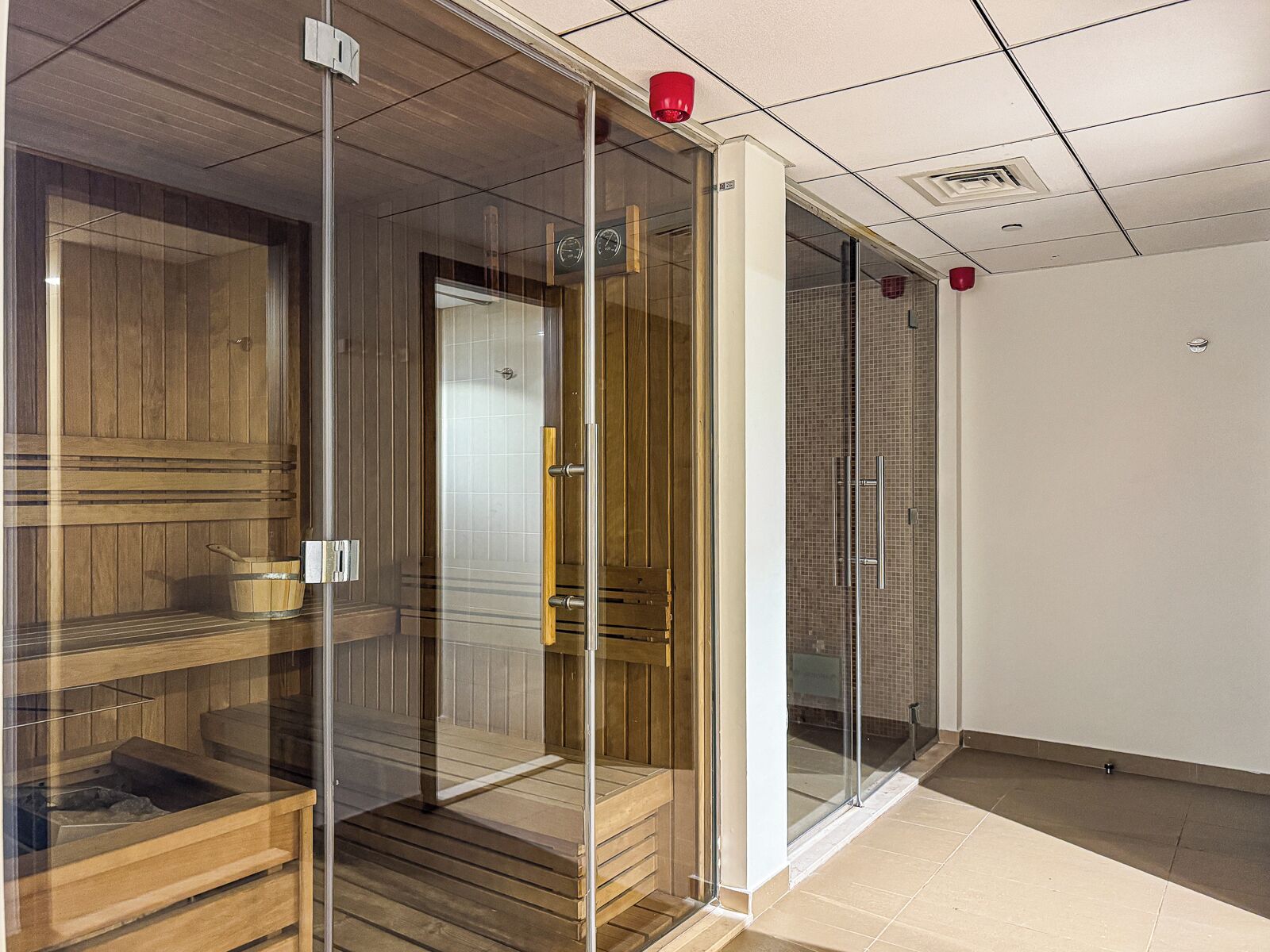 A sauna room with wooden benches, a glass door, and a tiled floor.