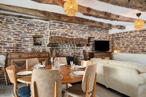 Un comedor con pared de piedra, vigas de madera, chimenea y televisor.